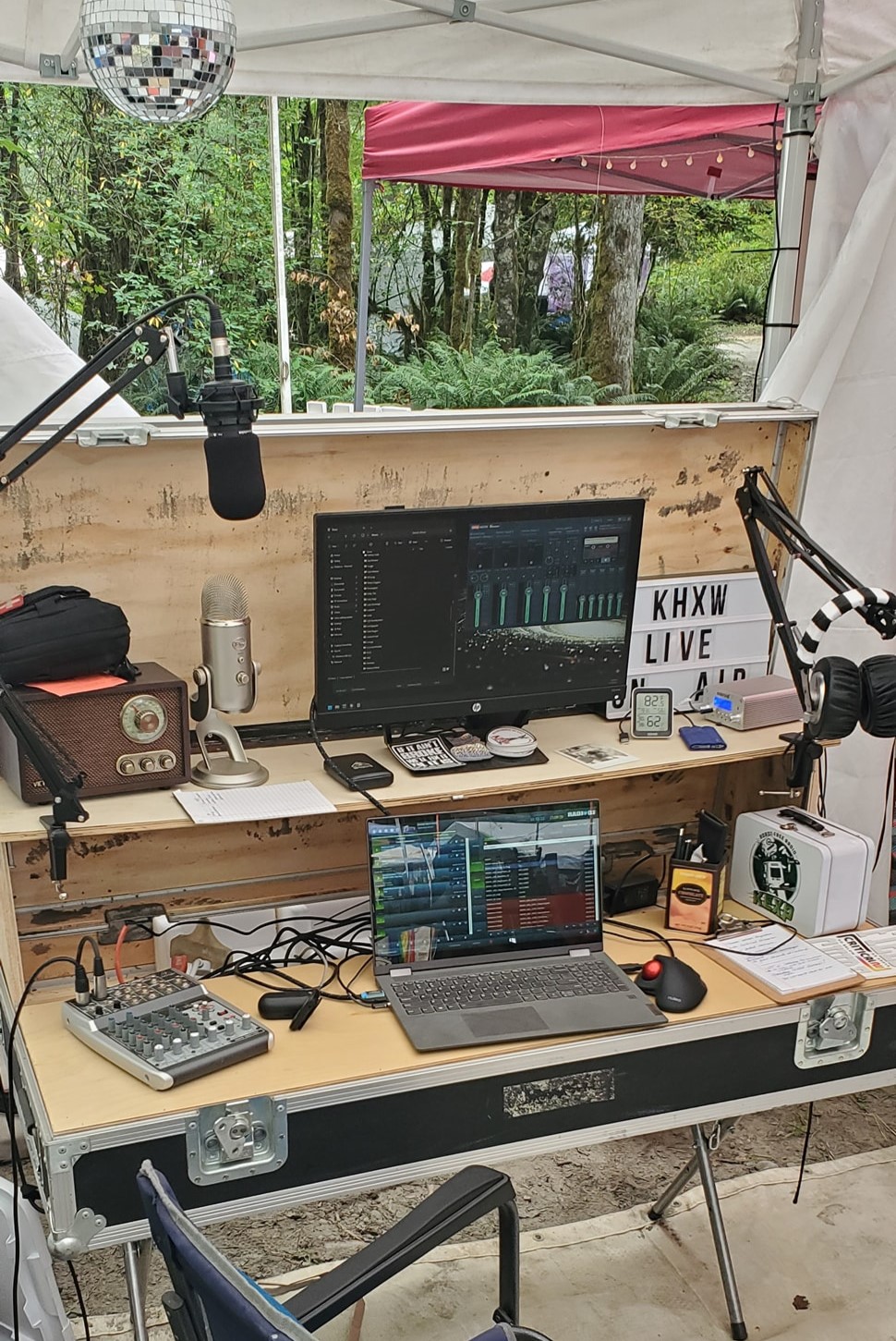 A view of a portable workstation set up in the forest, containing a laptop, microphones, mixer, speakers, and other equipment.